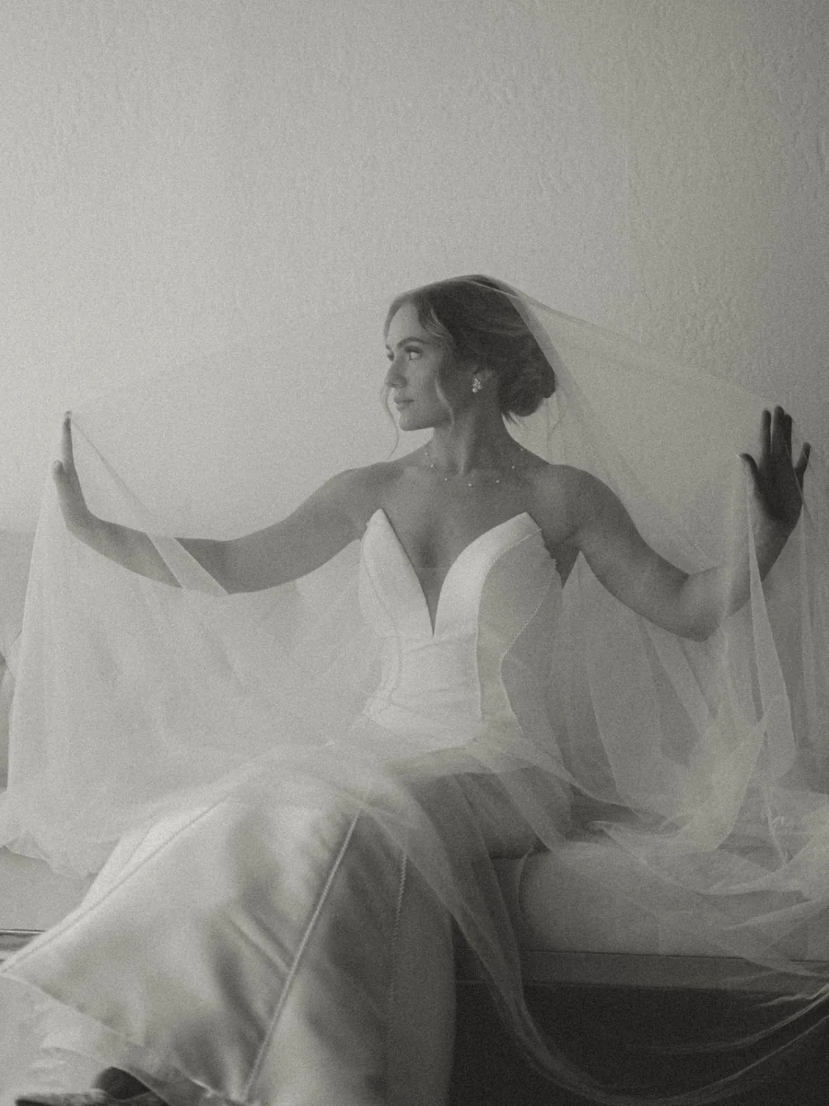 A seated bride lifting her veil, in black and white